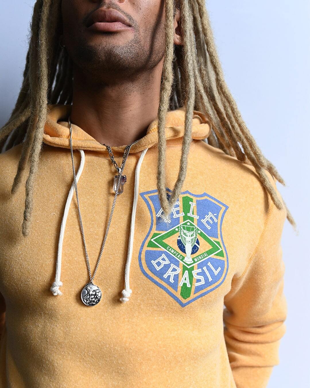 Person in a Pele yellow hoodie with a 'Pele Brasil' emblem and wearing necklaces.